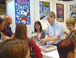 Michael Dowling (in striped shirt) and former ALA President Loriene Roy (right) assist IFLA attendees at the ALA exhibit booth in Singapore. Photo by Carlon Walker