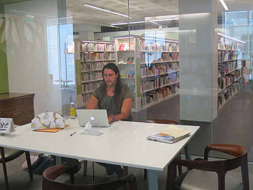 Z! Haukeness from the Shine Initiative—a nonprofit based in Madison, Wisconsin—keeps a prominent profile in a glass room in the middle of Madison Public Library, where he and a coworker spend 30 hours a week helping patrons find housing and jobs and apply for food stamps. Some people come just to talk through hardships, he says. Photo: Ellyn Ruhlmann