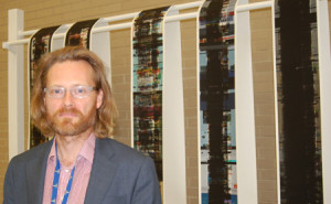 Matthew Mann, curator of the "UNCENSORED: Information Antics" exhibit, stands in front of an installation by artist Nancy Daly, a series of five individual pieces based on computer printouts of Google searches titled <em>About 286,000,000 Results.</em>