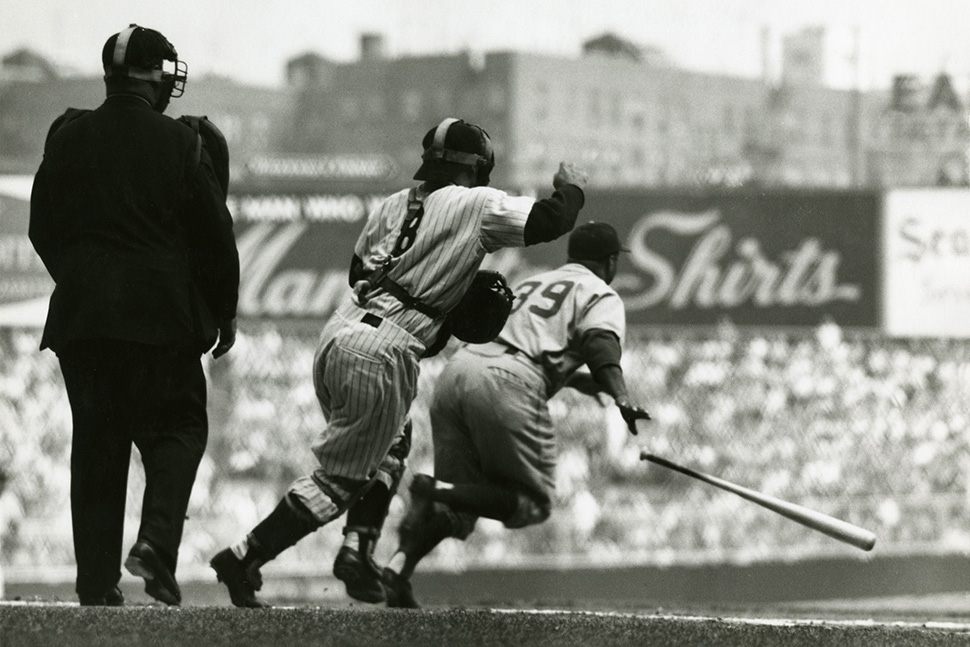 At Yankee Stadium during the 1955 World Series, Brooklyn batter Roy Campanella and New York catcher Yogi Berra both start toward first base: Campy attempting to beat out his grounder and Yogi preparing to back up the play.