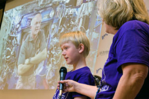 Fifth-grader Evan Sass asks NASA astronaut Jeff Williams a question via video chat while Denise Raleigh, Gail Borden Public Library's division chief of public relations and development, holds the microphone. The Elgin, Illinois, library was one of eight nationwide selected for the traveling exhibit, Discover Space: A Cosmic Journey. Photo: Jason Brown