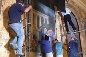 A team returns a restored mural to the wall in Boston Public Library’s Bates Hall.