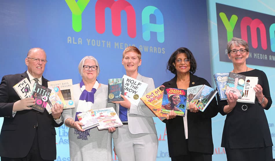 At the Youth Media Awards, from left: ALA President Jim Neal, Reforma President Tess Tobin, Association of Library Service to Children President Nina Lindsay, Coretta Scott King Awards Chair Claudette McLinn, and Young Adult Library Services Association President Sandra Hughes-Hassell display the winning books. <span class="credit">Photo: Cognotes</span>