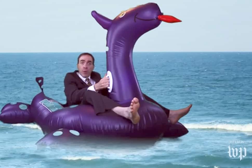 Ron Charles is wearing a full suit sitting on an inflatable dragon pool toy.