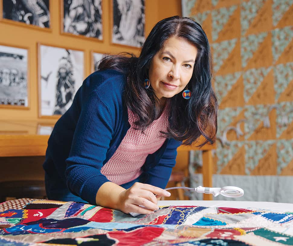 Archivist Tawa Ducheneaux stands over a quilt that dates to between 1913–1915. Each square was created by quilting club members from the Wounded Knee ­District in South Dakota and notes the maker’s identity, the date, and sometimes the family’s cattle brand.