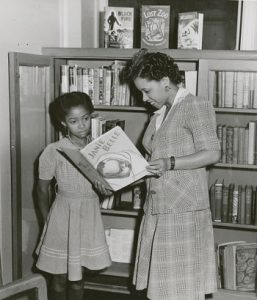 Librarian Augusta Baker showing a copy of Ellen Tarry's "Janie Belle" to a young girl, at the 135th Street (now Countee Cullen) Branch Library of the New York Public Library in Harlem, New York, around 1941. Courtesy NYPL