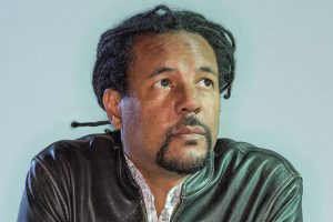 Colson Whitehead (Black man with braided hair pulled back, wearing leather jacket, looking just up and to the right)