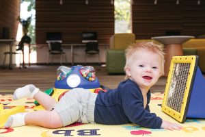 A toddler at Arlington Heights (Ill.) Memorial Library (AHML) enjoys tummy time while playing with Peek-a-Boo Mirror, a sensory toy in AHML’s collection.