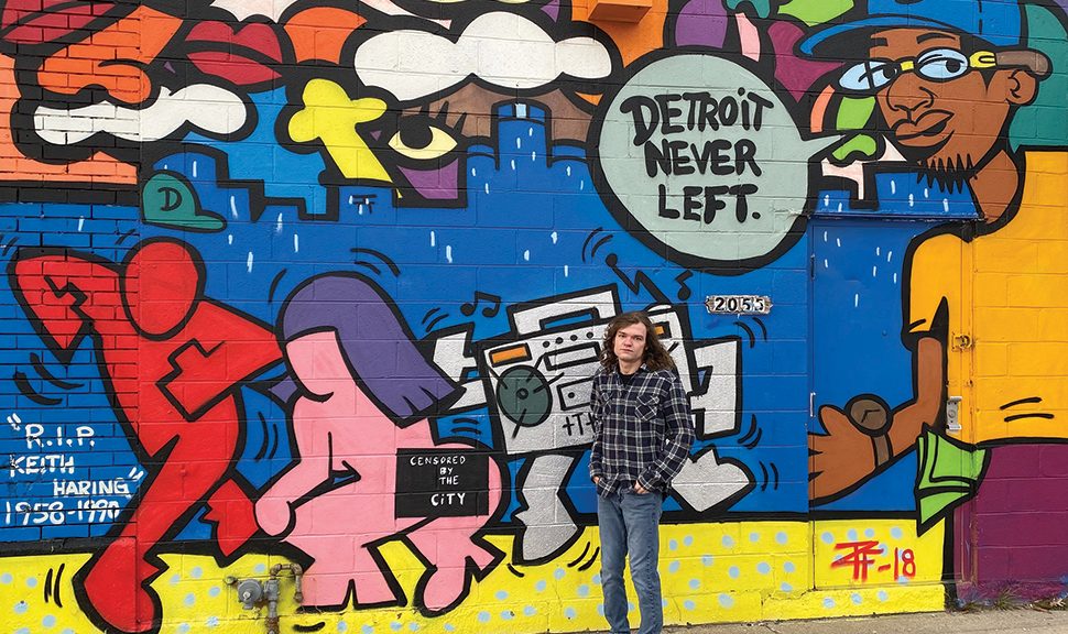 Photo of Cameron Socha, who graduates this year from Wayne State University’s School of Information Sciences, posing in front of a mural in Detroit. He collaborated with his professor Joan Beaudoin to catalog local murals.