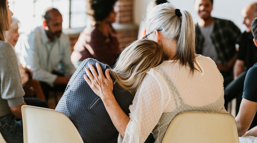 Stock image of two women leaning on one another in a support group.
