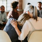 Stock image of two women leaning on one another in a support group.