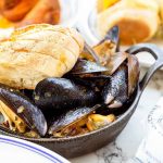 Cast iron bowl of mussels with sliced bread on top