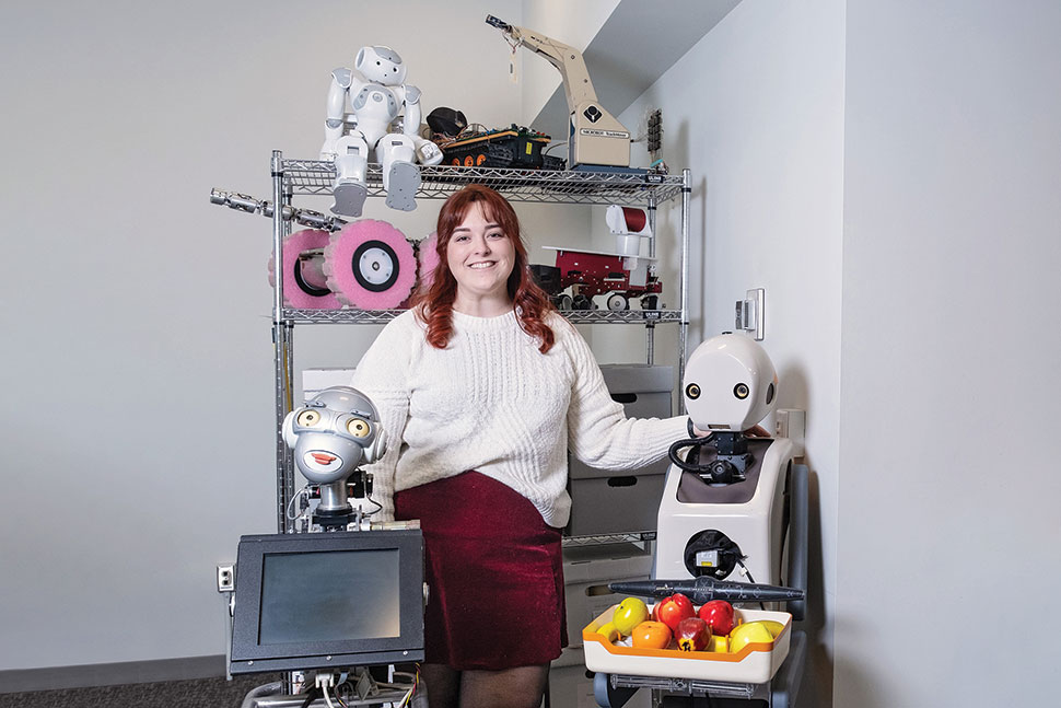 Kathleen Donahoe, robot archive processing archivist at Carnegie Mellon University (CMU), poses with a selection of robots in CMU's archive.
