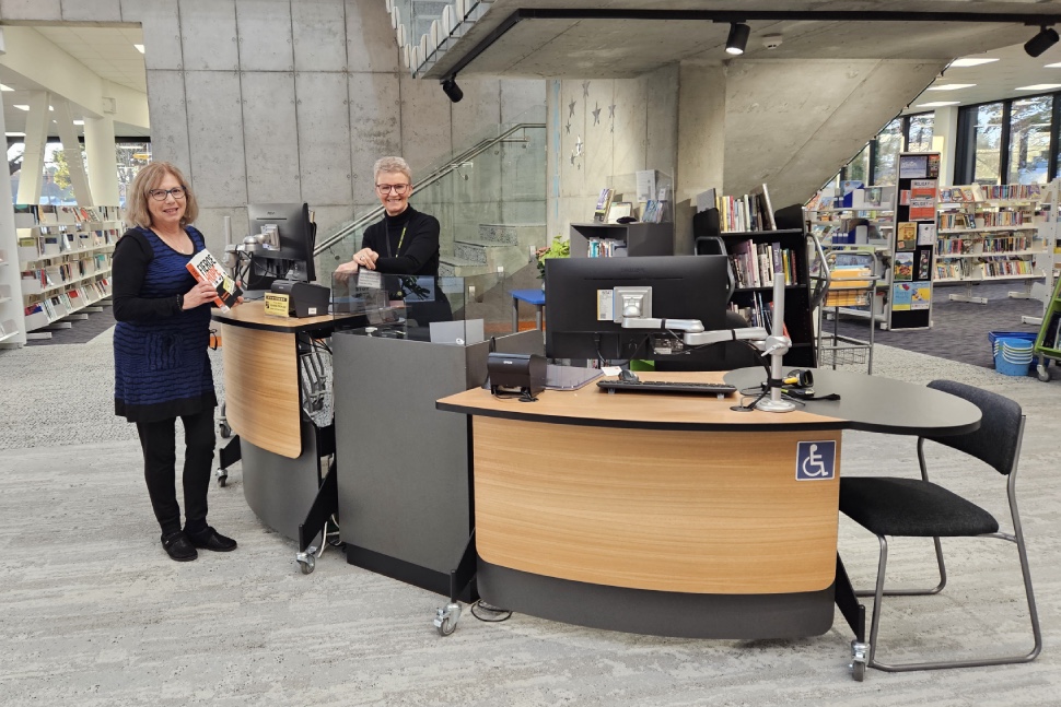 Two library workers stand at a rounded desk in a modern-looking library