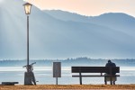 Lone person on a bench in front of an imposing lake and mountain.