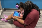 Woman with a young girl in her lap, both looking at a tablet computer