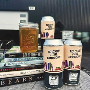 Stacked on top of books about bears are cans that say "To Chai For Kombucha" and a mason jar full of the tea.