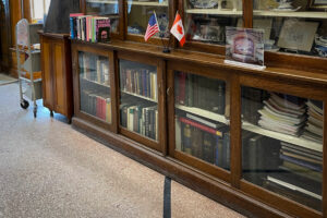 A black line on the floor inside the Haskell Library indicates the border between the US and Canada. Above the line, a small US flag on the left and Canadian flag on the right sit side-by-side on a bookshelf.
