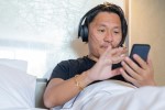 A man in bed with headphones and a phone