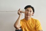 A man holding a tin can on a string up to his ear