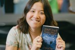 Author Leanne Su holds up a paperback book with a blue cover and the title and her name in yellow.