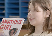Girl holding up the book Ambitious Girl in a screencap from The ABCs of Book Banning