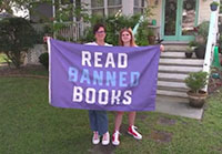Two people with a banner saying Read Banned Books in a screencap from Banned Together