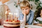 Sad-looking boy glaring at a birthday cake alone