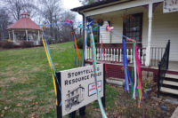The "sunbrella," a bare-spoked umbrella with ribbons and bells hanging from its spokes, standing over the Storytelling Resource Center sign in front of its building.