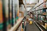 Boy examining books on library shelves